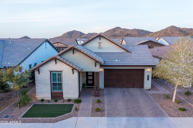 view of front facade with a mountain view, a garage, a tile roof, stone siding, and decorative driveway