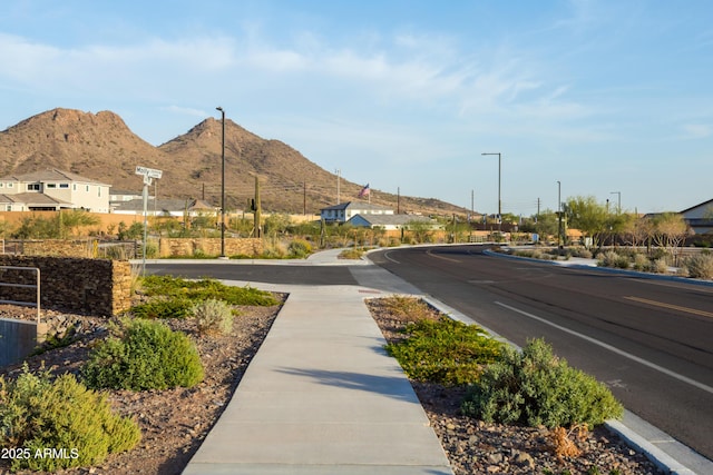 view of road with curbs, a mountain view, sidewalks, and street lights