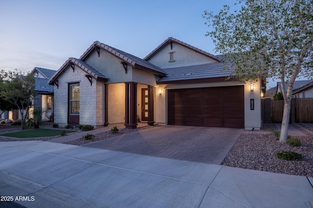 view of front of property with stone siding, an attached garage, fence, decorative driveway, and stucco siding