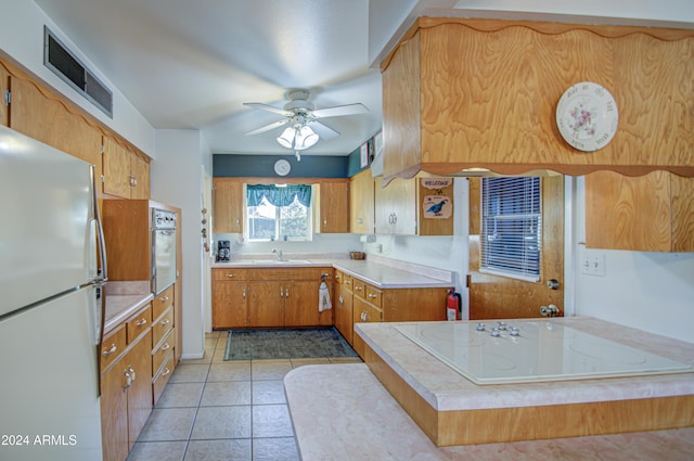 kitchen with white appliances, sink, ceiling fan, light tile patterned floors, and kitchen peninsula