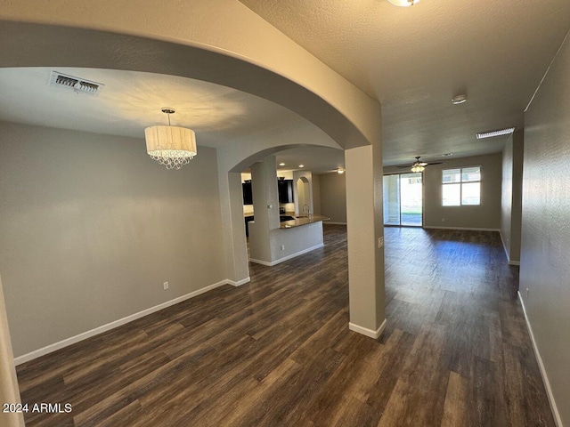 unfurnished room with a textured ceiling, ceiling fan with notable chandelier, and dark wood-type flooring