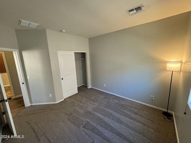 unfurnished bedroom with dark colored carpet, a textured ceiling, and a closet