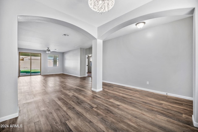 unfurnished living room featuring ceiling fan with notable chandelier and dark wood-type flooring