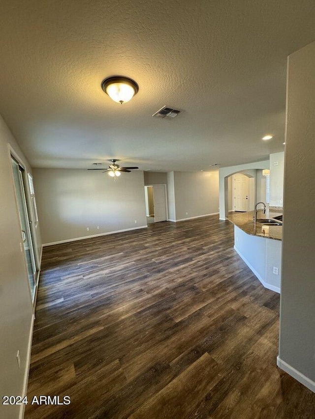 unfurnished living room with sink, ceiling fan, dark hardwood / wood-style flooring, and a textured ceiling