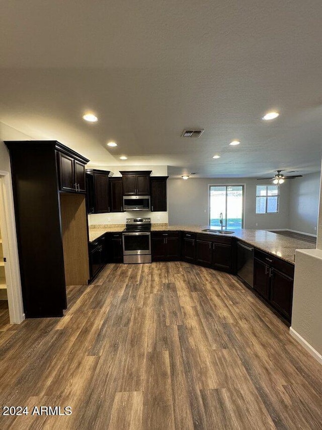 kitchen featuring dark hardwood / wood-style flooring, light stone counters, stainless steel appliances, ceiling fan, and sink