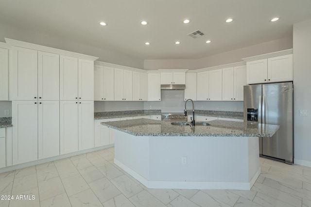 kitchen featuring white cabinetry, stone counters, sink, stainless steel fridge, and a kitchen island with sink