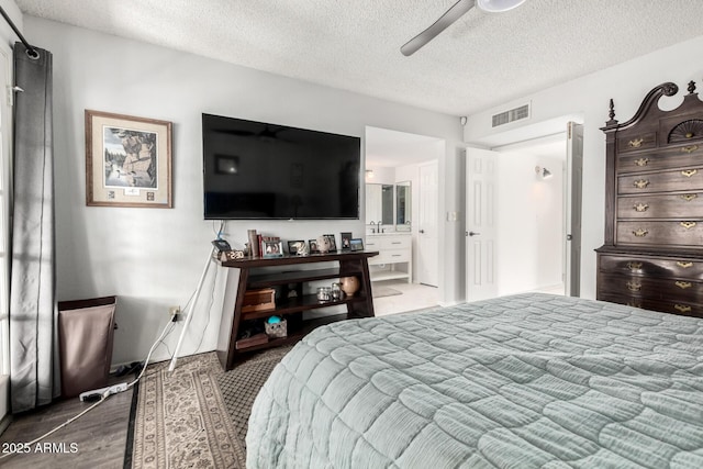 bedroom featuring a ceiling fan, a textured ceiling, visible vents, wood finished floors, and connected bathroom