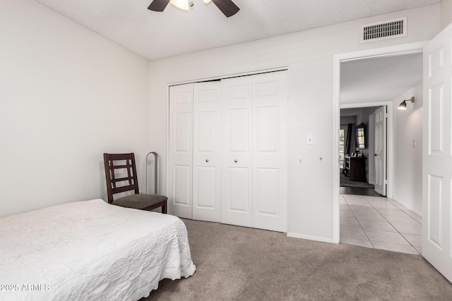 bedroom featuring ceiling fan, light colored carpet, visible vents, light tile patterned floors, and a closet