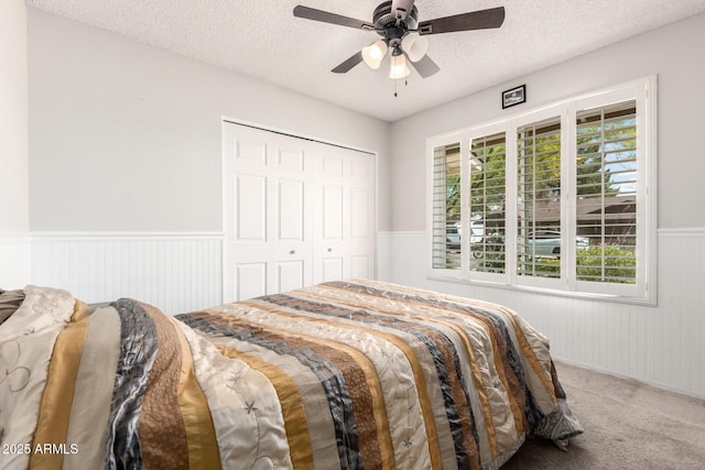 carpeted bedroom featuring a closet, a textured ceiling, ceiling fan, and a wainscoted wall