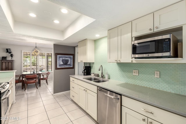 kitchen with backsplash, a sink, light tile patterned floors, baseboards, and stainless steel appliances