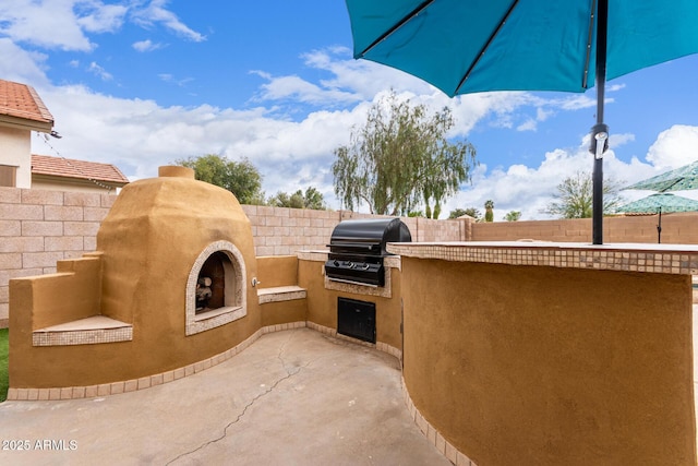 view of patio with a grill, a fenced backyard, exterior fireplace, and an outdoor kitchen