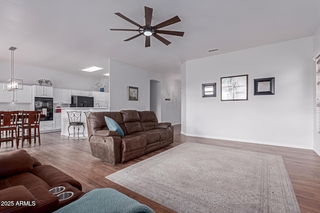 living area featuring light wood-style flooring, visible vents, arched walkways, and baseboards