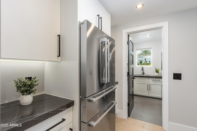 kitchen featuring dark countertops, recessed lighting, freestanding refrigerator, white cabinetry, and a sink