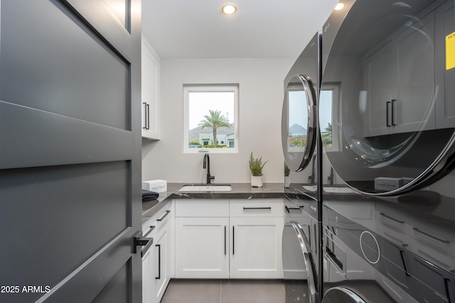 laundry area featuring light tile patterned floors, stacked washer / drying machine, recessed lighting, cabinet space, and a sink