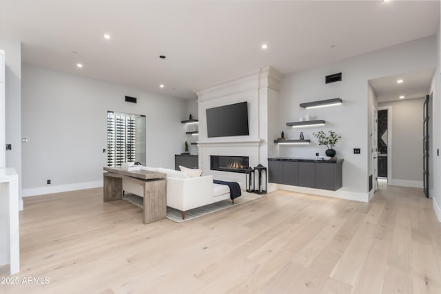 living room with visible vents, baseboards, a glass covered fireplace, light wood-style flooring, and recessed lighting