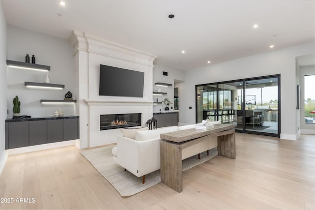 living area with baseboards, light wood finished floors, a glass covered fireplace, and recessed lighting