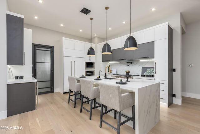 kitchen featuring a breakfast bar area, stainless steel appliances, decorative backsplash, modern cabinets, and light wood-type flooring