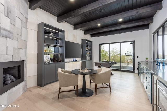 dining space with light wood-type flooring, a tile fireplace, wooden ceiling, and beamed ceiling