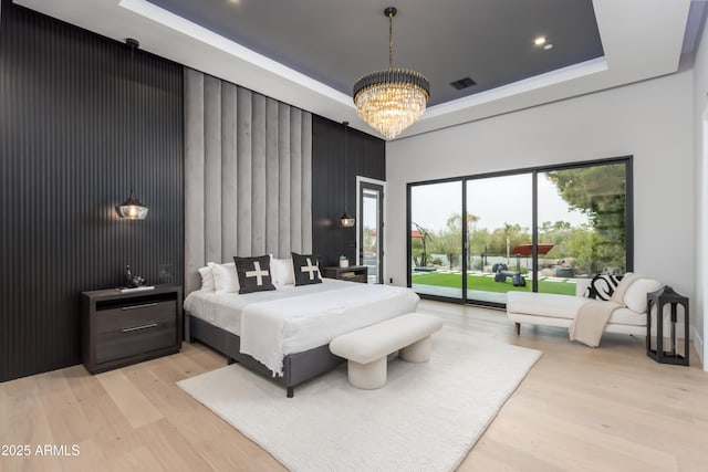 bedroom with a tray ceiling, access to outside, visible vents, and light wood finished floors