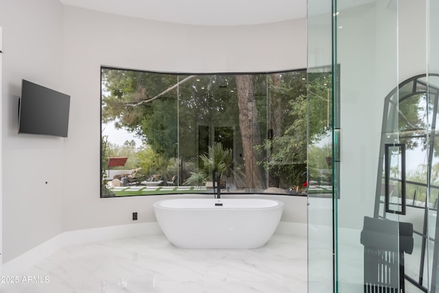 bathroom with marble finish floor, a freestanding tub, and baseboards