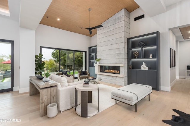 living room with a high ceiling, light wood-type flooring, wooden ceiling, baseboards, and a tile fireplace