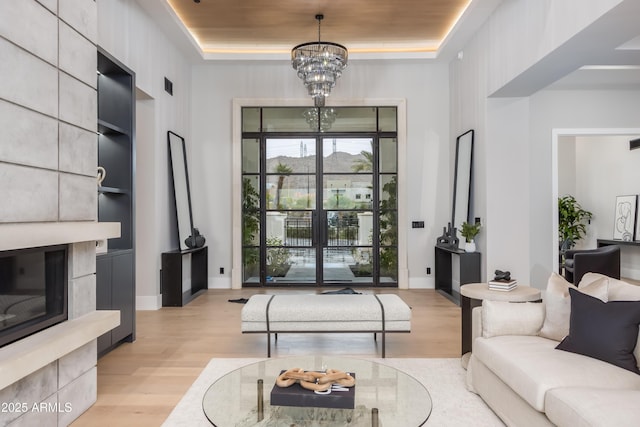 living room featuring baseboards, a tiled fireplace, an inviting chandelier, a tray ceiling, and light wood-style floors