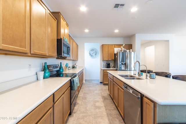 kitchen featuring stainless steel appliances, a sink, light countertops, recessed lighting, and a kitchen island with sink