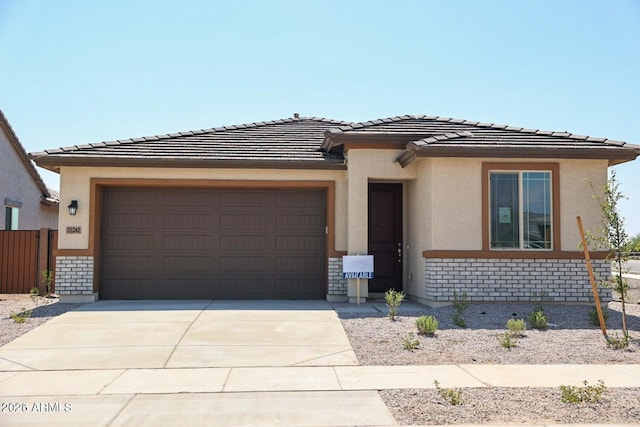 prairie-style house featuring stucco siding, a tile roof, fence, concrete driveway, and an attached garage