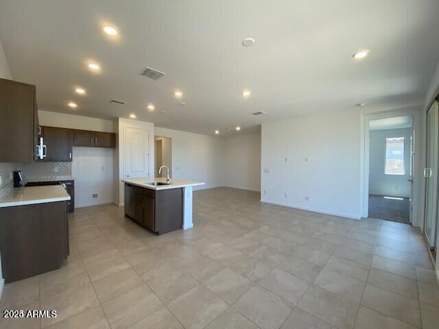 kitchen featuring visible vents, a kitchen island with sink, a sink, dark brown cabinetry, and light countertops