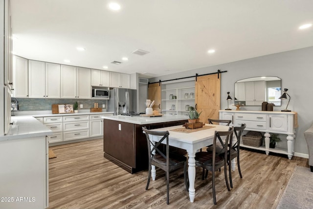 4840 E Sunnyside Dr, Scottsdale, AZ 85254 - kitchen featuring a barn door, decorative backsplash, light wood-style flooring, light countertops, and appliances with stainless steel finishes