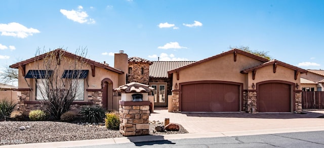 mediterranean / spanish-style home featuring stone siding, a tiled roof, an attached garage, stucco siding, and driveway