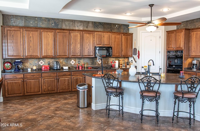 kitchen featuring a breakfast bar, decorative backsplash, a sink, black appliances, and brown cabinets