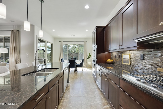 kitchen with a sink, appliances with stainless steel finishes, decorative backsplash, dark stone countertops, and decorative light fixtures