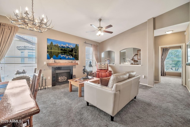 carpeted living room featuring ceiling fan with notable chandelier, baseboards, a glass covered fireplace, and lofted ceiling