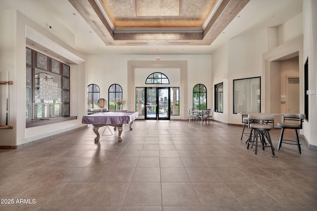 game room featuring baseboards, a towering ceiling, ornamental molding, tile patterned floors, and a tray ceiling