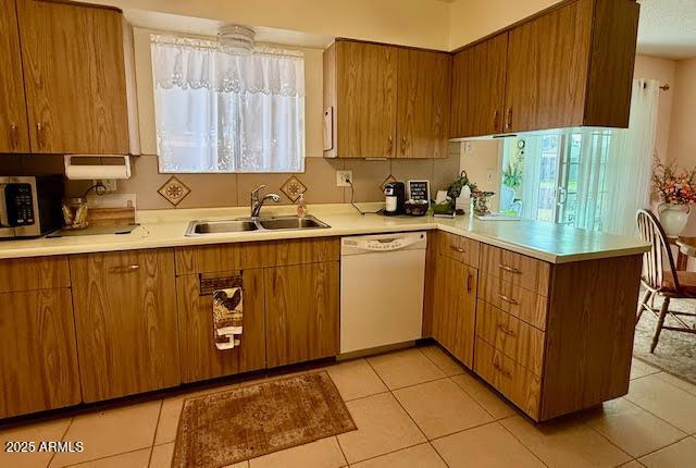 kitchen with light countertops, stainless steel microwave, white dishwasher, a sink, and a peninsula