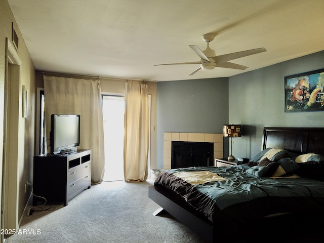 carpeted bedroom with a tiled fireplace and ceiling fan