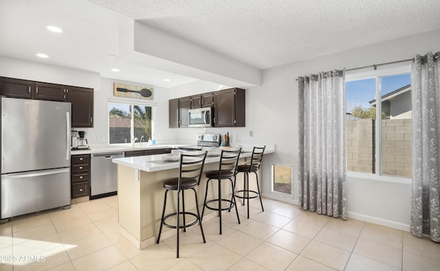 kitchen with stainless steel appliances, plenty of natural light, a breakfast bar area, and a textured ceiling