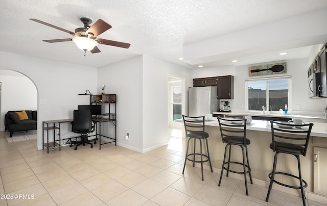 kitchen featuring light tile patterned flooring, appliances with stainless steel finishes, a kitchen breakfast bar, dark brown cabinets, and a textured ceiling