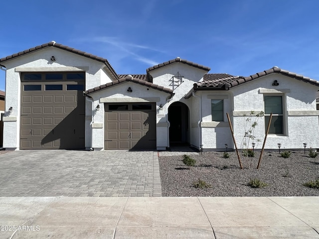 mediterranean / spanish-style home with an attached garage, stucco siding, driveway, and a tiled roof