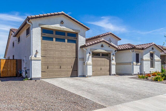 mediterranean / spanish-style home featuring decorative driveway, stucco siding, a tile roof, and fence