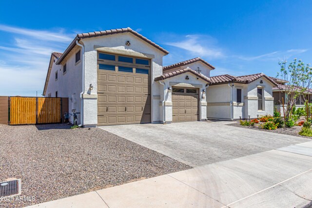 mediterranean / spanish house with a tiled roof, decorative driveway, fence, an attached garage, and stucco siding
