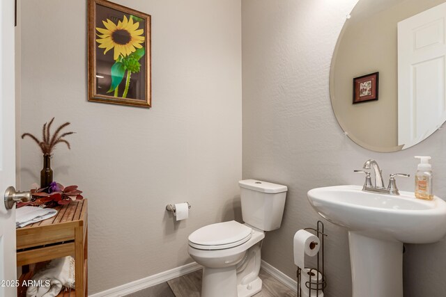 half bath with baseboards, toilet, and wood finished floors