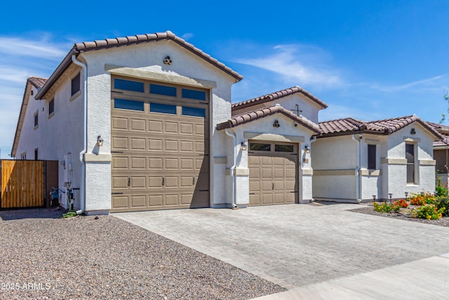 mediterranean / spanish-style home featuring decorative driveway, stucco siding, a tile roof, and fence