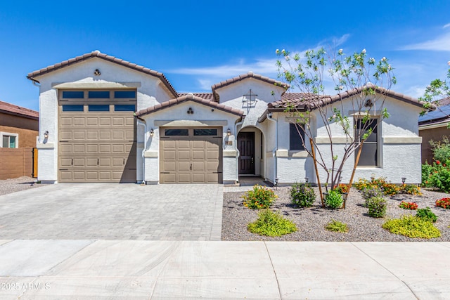 mediterranean / spanish-style home with a garage, stucco siding, a tile roof, and decorative driveway