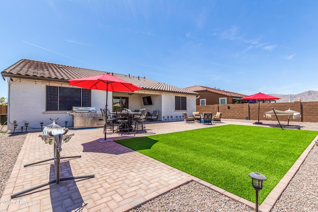 rear view of house with fence, a tile roof, brick siding, a patio, and a yard