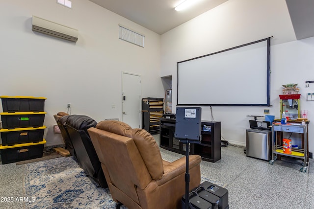 home theater with a towering ceiling, baseboards, speckled floor, a wall mounted AC, and water heater