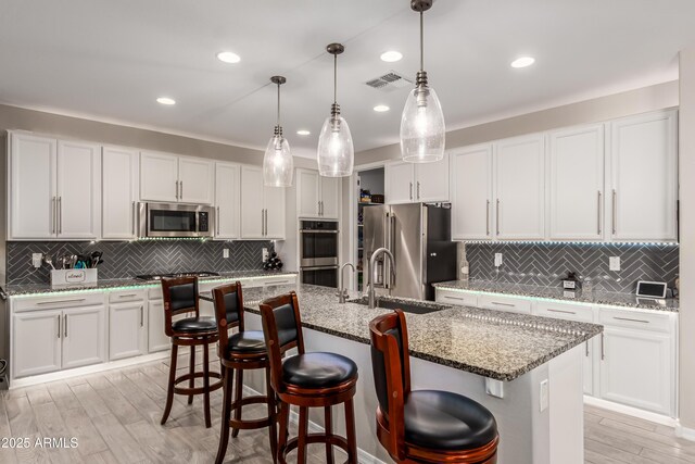 kitchen with white cabinets, a sink, stainless steel appliances, decorative backsplash, and visible vents