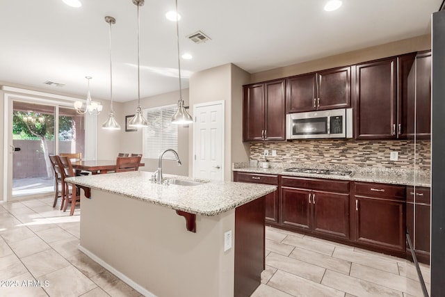 kitchen featuring backsplash, a center island with sink, sink, appliances with stainless steel finishes, and decorative light fixtures