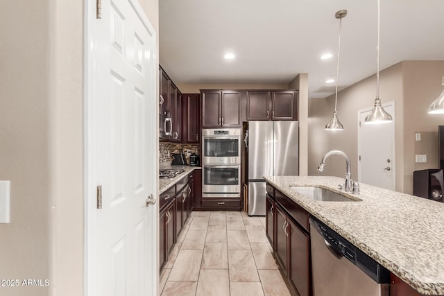 kitchen featuring appliances with stainless steel finishes, dark brown cabinets, sink, pendant lighting, and a center island with sink